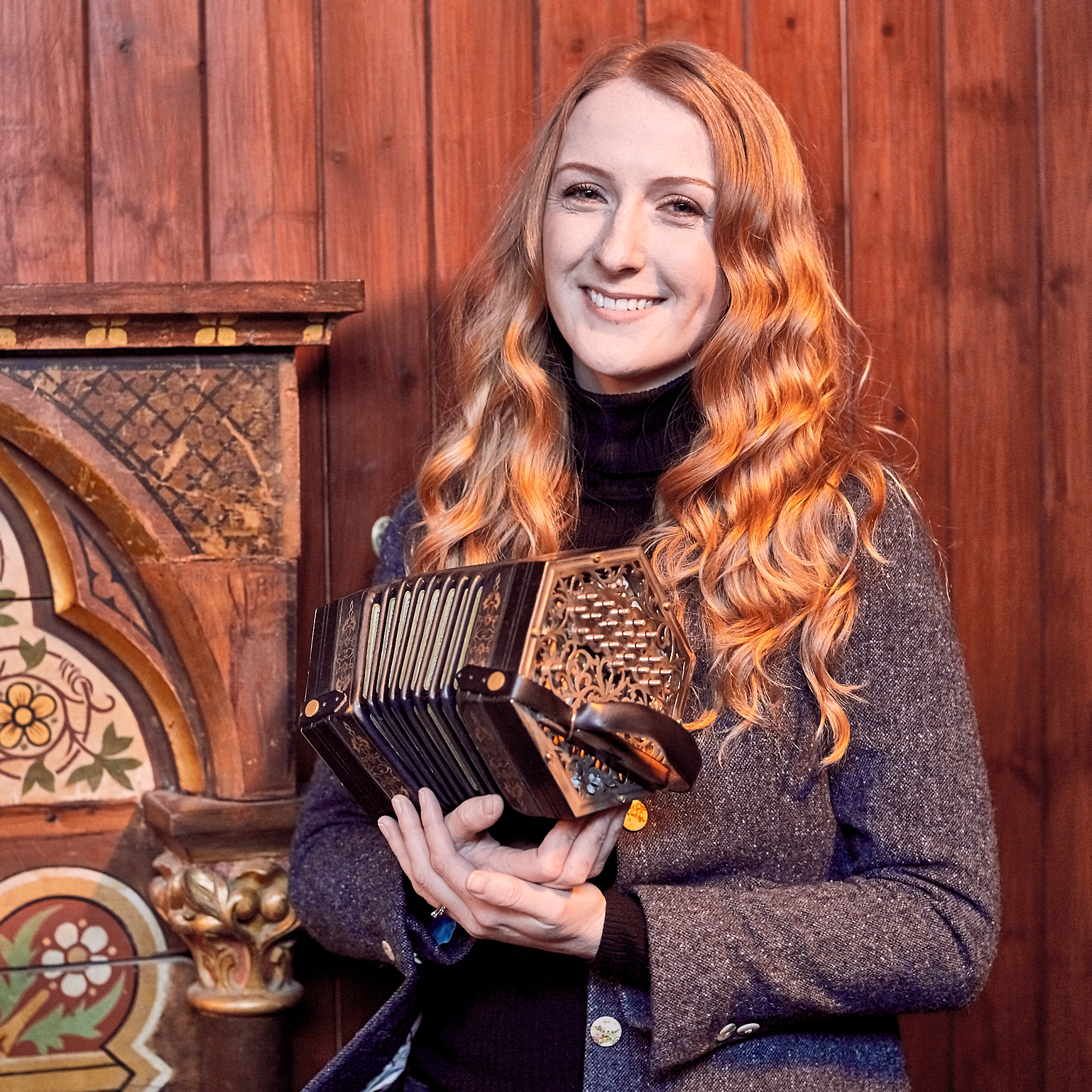 Caitlín Nic Gabhann holding a concertina while smiling at the camera.